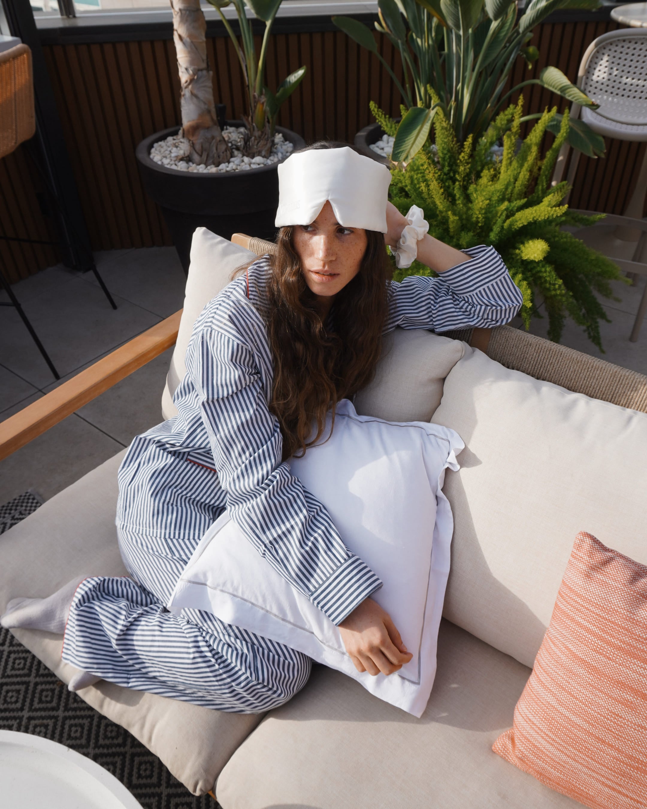 Woman wearing a white silk sleep mask by Noemus while resting on a sofa