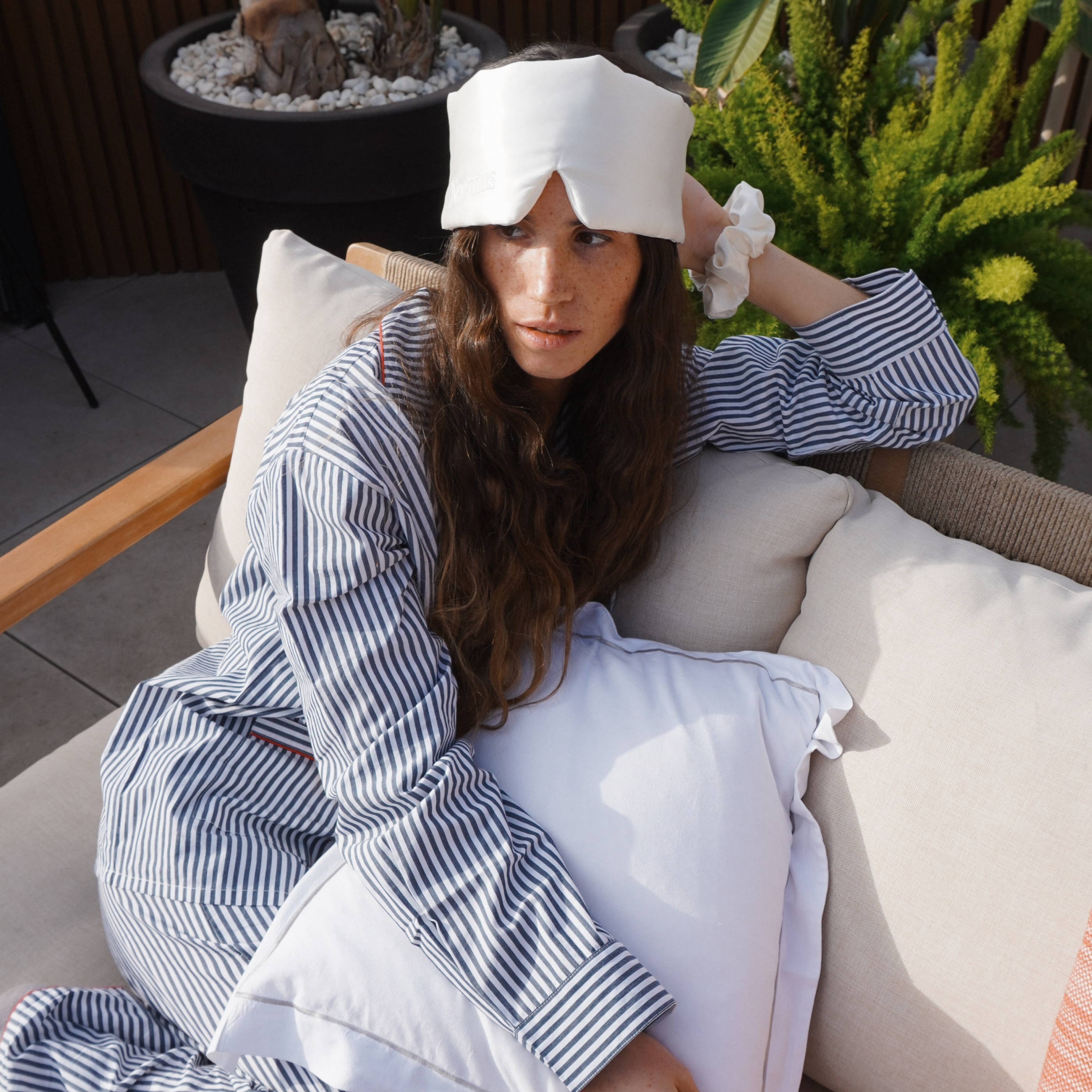 Woman wearing a white silk sleep mask by Noemus while relaxing outdoors